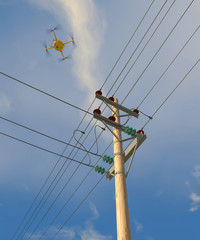 UAV drone in flight inspecting high-voltage electrical distribution wires on wooden poles. Fictitious UAV; overcast sky and motion blur for dramatic effect.