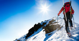 Fototapeta  - Ski mountaineer walking up along a steep snowy ridge with the sk