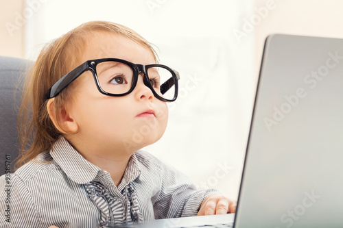 Fényképezés Smart toddler girl wearing big glasses while using her laptop