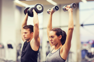 Canvas Print - smiling man and woman with dumbbells in gym