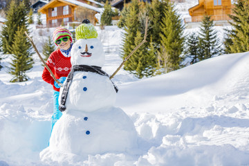 Wall Mural - Winter fun, happy girl playing with snowman with a mustache