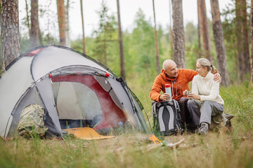 Two campers talking to each other and drinking tea by a tent in