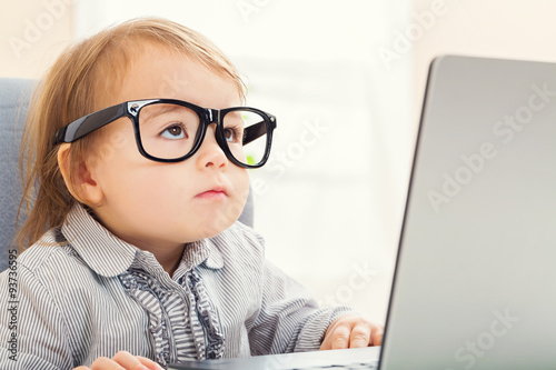 Fotomural Intelligent toddler girl wearing big glasses while using her laptop