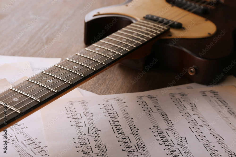 Electric guitar with music notes on wooden table close up