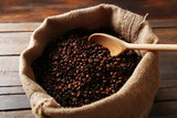 Fototapeta Storczyk - Sac with roasted coffee beans with spoon on wooden background