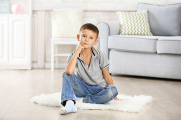 Little boy sitting on carpet, on home interior background