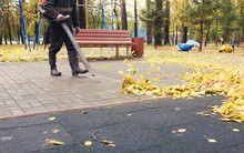 Worker Cleaning Playground In The Autumn Park From Dead Leaves With A Blower