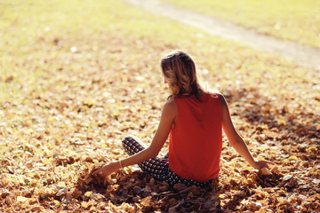 Wall Mural - girl sits resting in a park on the fallen leaves