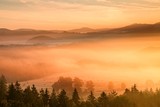 Fototapeta Na ścianę - Pink daybreak in hilly landcape. Autumn freeze misty morning in a beautiful hills. Peaks of hills are sticking out from pink orange fog