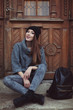 Happy young smiling hipster woman sitting near the door. Street fashion concept. Toned