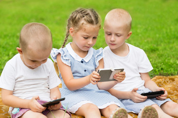 Happy children using smartphones sitting on the grass