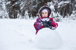 © Kekyalyaynen - Pretty girl in winter clothes rolling snowball for snowman making, winter