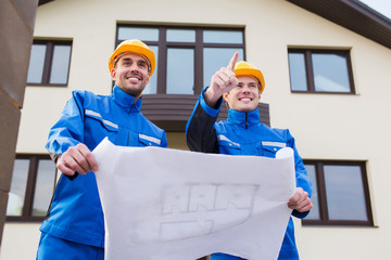 Wall Mural - smiling builders with blueprint pointing finger