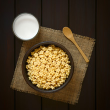 Honey Flavored Breakfast Cereal In Rustic Bowl With A Glass Of Milk And A Wooden Spoon On The Side, Photographed Overhead On Dark Wood With Natural Light