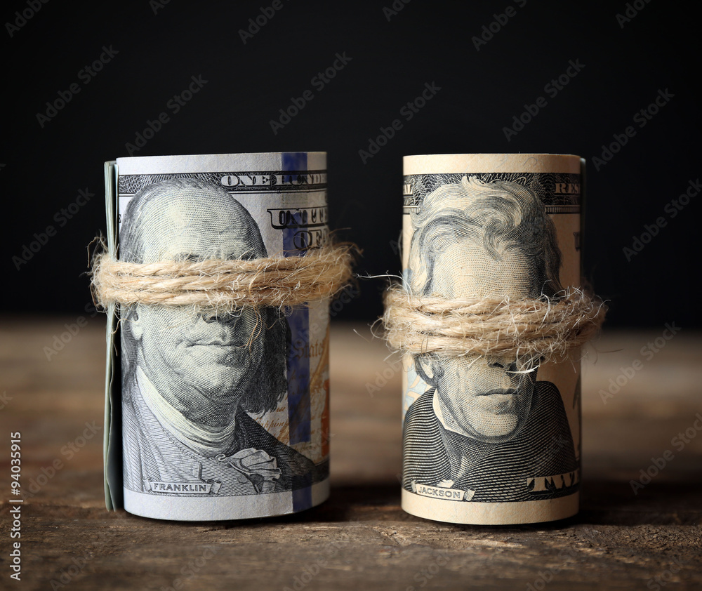 Dollars roll on wooden table in front of dark background