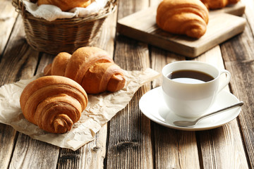 Wall Mural - Tasty croissants with cup of coffee on brown wooden background