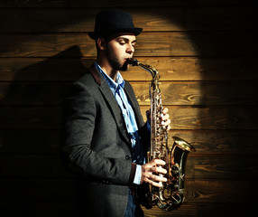 Wall Mural - Elegant saxophonist plays jazz on wooden background