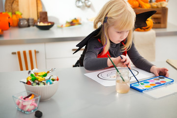 Wall Mural - Interested halloween dressed girl drawing pumpkin Jack-O-Lantern