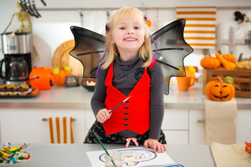 Wall Mural - Girl in halloween bat costume drawing Jack-O-Lantern on paper