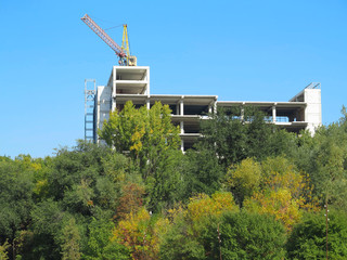 Crane and building construction site against blue sky and trees