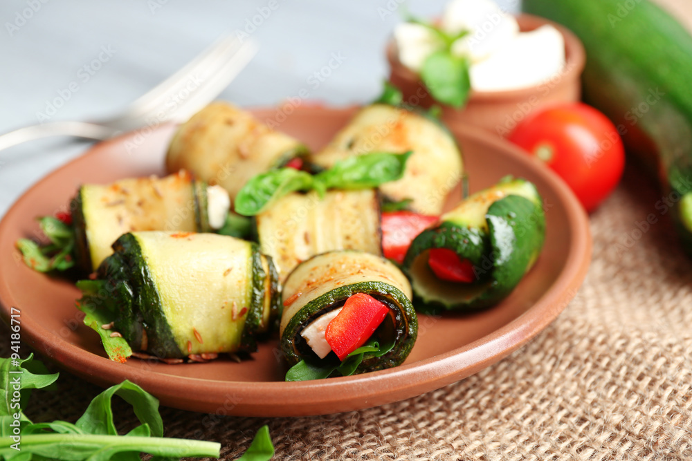 Salad with arugula and zucchini rolls on plate, on table background