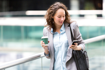 Young attractive business woman using smartphone drinking coffee