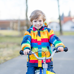 Poster - kid boy in safety helmet and colorful raincoat riding bike, outd