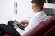 © COSPV - Smiling young businessman holding a tablet at sofa in office sit