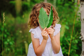 child girl exploring nature and playing with leaves in summer forest