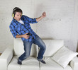 20s or 30s man jumped on couch listening to music on mobile phone with headphones playing air guitar