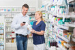 © Tyler Olson - Happy Customer Using Mobile Phone While Chemist Holding Products