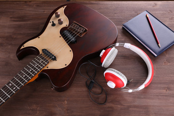 Canvas Print - Electric guitar with headphones and notebook on wooden table close up