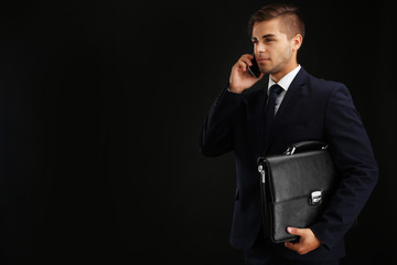 Wall Mural - Elegant man in suit with briefcase on dark background