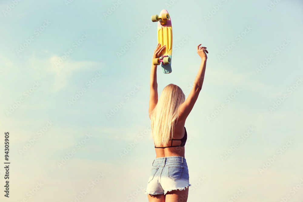 Young woman with skating board on blue sky background