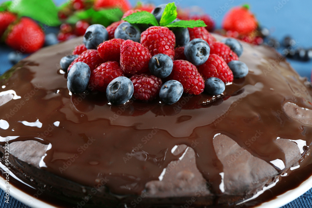 Delicious chocolate cake with summer berries on blue tablecloth, closeup