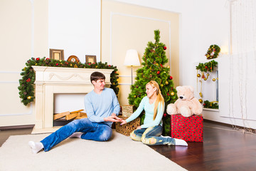 Nice love couple sitting on carpet in front of fireplace. Woman and man celebrating Christmas