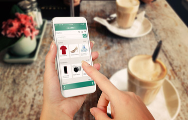 Poster - Smart phone online shopping in woman hand. Desk with caffe in background. Buy clothes shoes accessories with e commerce web site