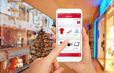 Poster - Smart phone online shopping in woman hand during Christmas. Shopping center in background. Buy clothes shoes accessories with e commerce web site