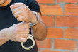 close-up shot man's hands unlocking handcuffs in front of terracotta brick blocks wall with copy-space
