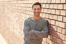 Friendly Guy Leaning Against A Textured Brick Wall Outdoors