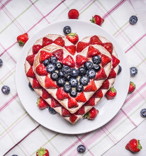 Homemade Cake With Strawberries And Blueberries For Valentine's Day Heart Shaped On A White Plate On A Striped Tablecloth With Scattered Around The Berries