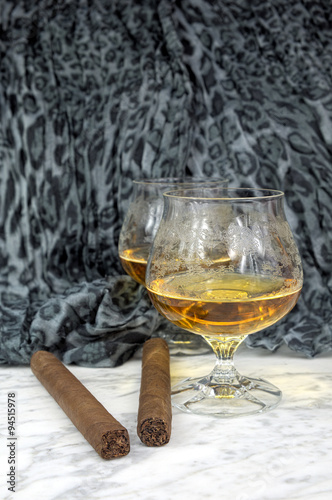 Naklejka dekoracyjna Two glasses of cognac with a cigar on a marble table