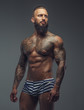 © Fxquadro - Tattooed muscular man with beard in stripes panties.