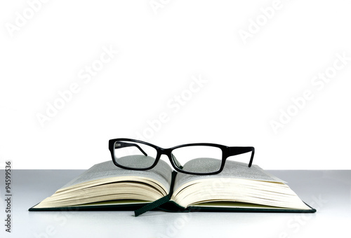 Fotografía Book and reading glasses on a white table and white background