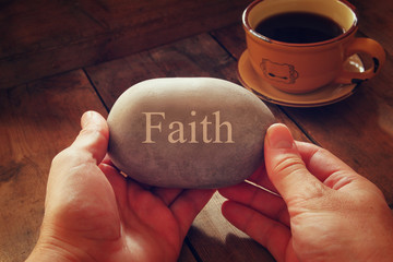 hands holding pebble stone with the word faith