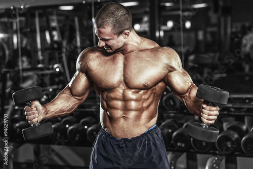 Nowoczesny obraz na płótnie Athlete muscular bodybuilder in the gym training biceps with dumbbells