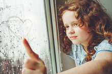 Happy Child Drawing Heart On The Window.