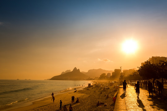 unidentifiable silhouettes enjoy late afternoon sun rays on ipanema beach in rio de janeiro, brazil.