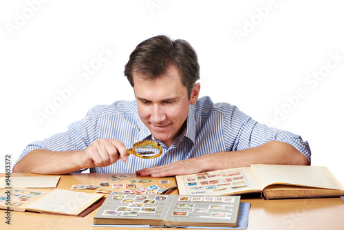 Fotomural Man watching a collection of postage stamps with magnifier