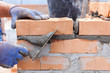 Construction mason worker bricklayer installing red brick with trowel putty knife outdoors